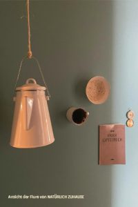 Eine alte Kaffeekanne, eine Tasse, eine kleine Schüssel, ein Gipfelbuch und ein Kompasse hängen an einer Wand